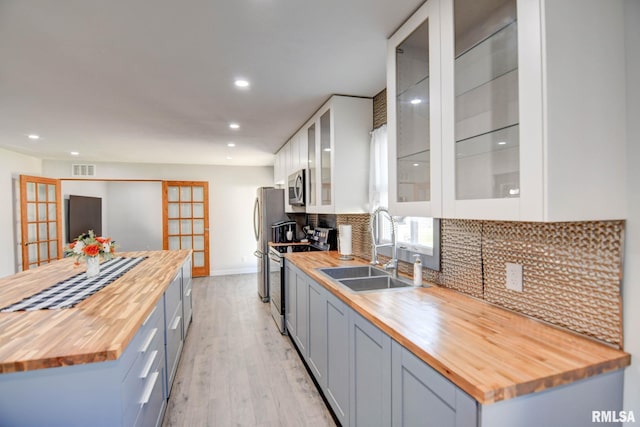 kitchen featuring appliances with stainless steel finishes, butcher block countertops, decorative backsplash, light hardwood / wood-style floors, and sink