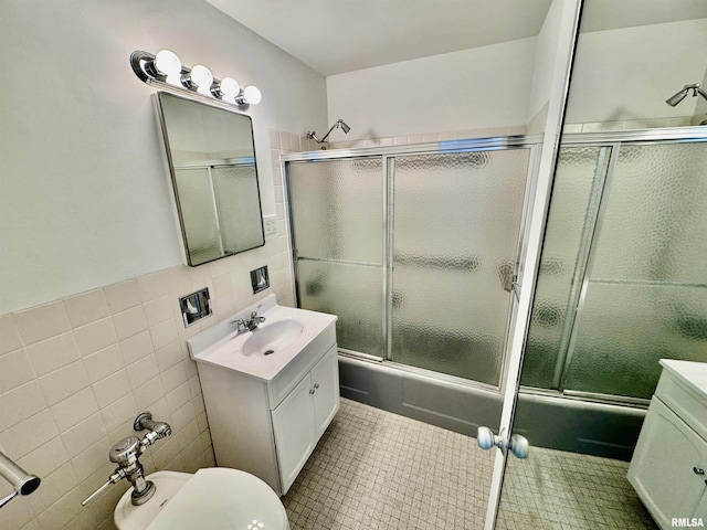 full bathroom featuring vanity, toilet, shower / bath combination with glass door, and tile walls