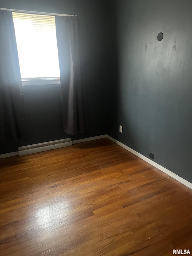 spare room featuring baseboard heating and wood-type flooring