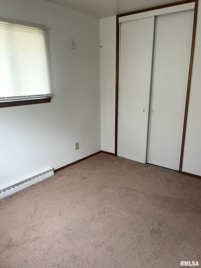 unfurnished bedroom with light colored carpet, a closet, and a baseboard heating unit