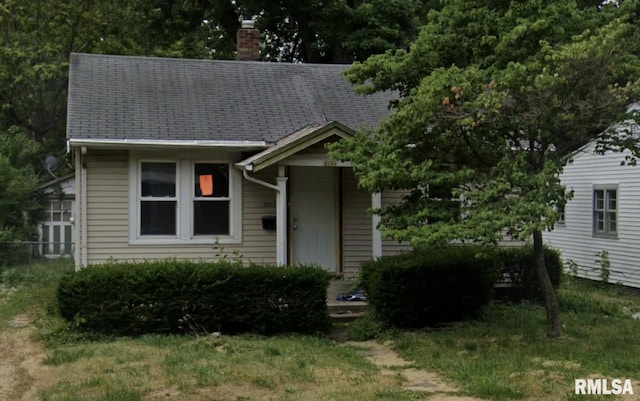 view of front of home featuring a shingled roof, a chimney, and a front yard