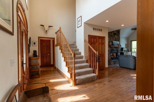 foyer entrance with hardwood / wood-style floors, a stone fireplace, and high vaulted ceiling