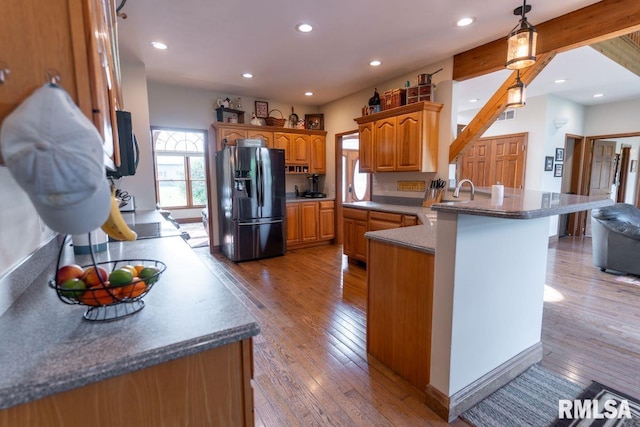 kitchen with a kitchen breakfast bar, kitchen peninsula, hanging light fixtures, light hardwood / wood-style flooring, and stainless steel fridge with ice dispenser