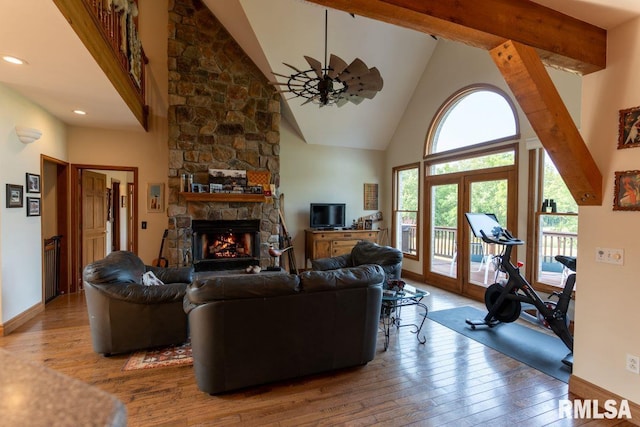 living room with hardwood / wood-style floors, high vaulted ceiling, a stone fireplace, ceiling fan, and beam ceiling