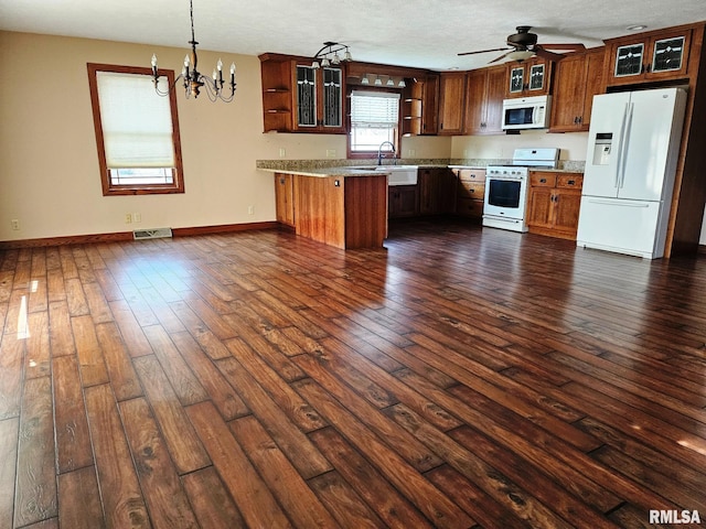 kitchen with kitchen peninsula, dark hardwood / wood-style flooring, white appliances, ceiling fan with notable chandelier, and sink