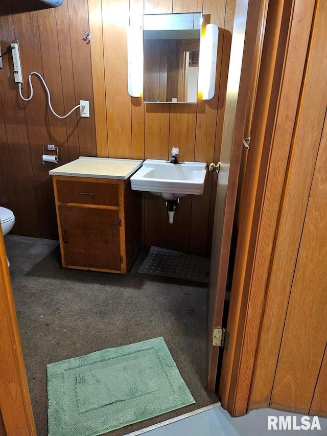 bathroom with wood walls, toilet, and sink