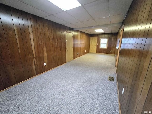 basement with wooden walls, a paneled ceiling, and carpet flooring