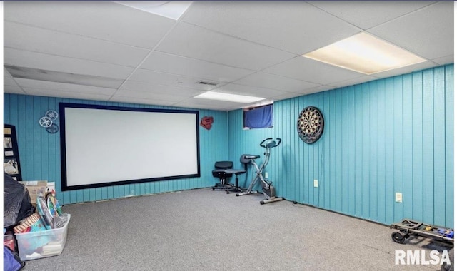 carpeted cinema featuring a paneled ceiling and wood walls