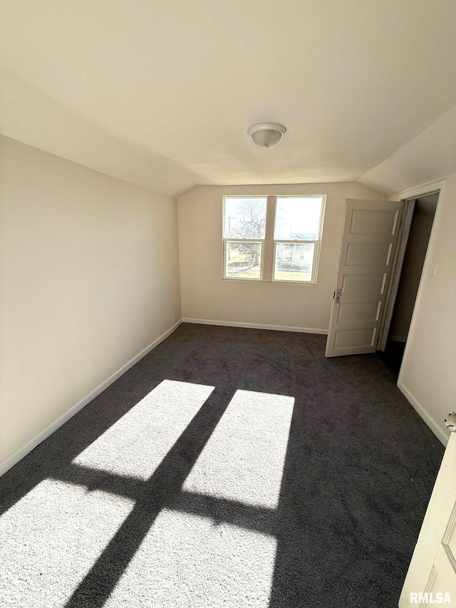 spare room featuring dark colored carpet and lofted ceiling