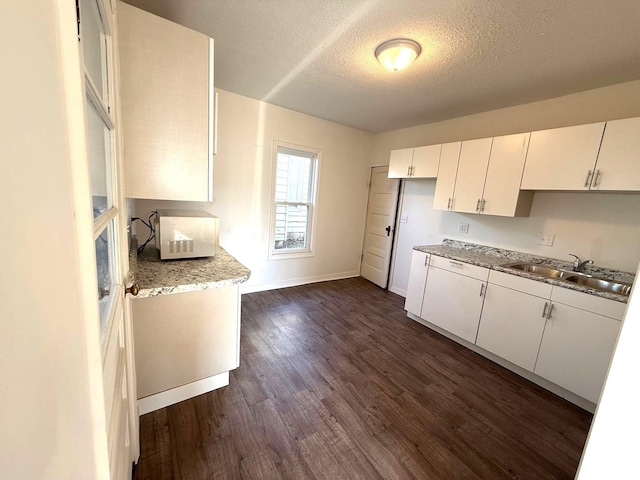 kitchen with light stone countertops, a textured ceiling, sink, dark hardwood / wood-style floors, and white cabinetry