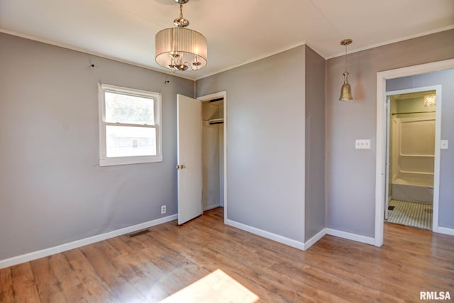 unfurnished bedroom with hardwood / wood-style floors, ornamental molding, and an inviting chandelier