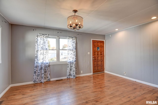 empty room featuring light hardwood / wood-style floors, wooden walls, and an inviting chandelier