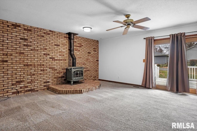 unfurnished living room with carpet flooring, a wood stove, a textured ceiling, and brick wall