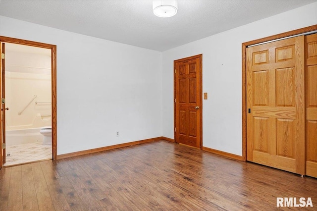 unfurnished bedroom with connected bathroom, wood-type flooring, and a textured ceiling