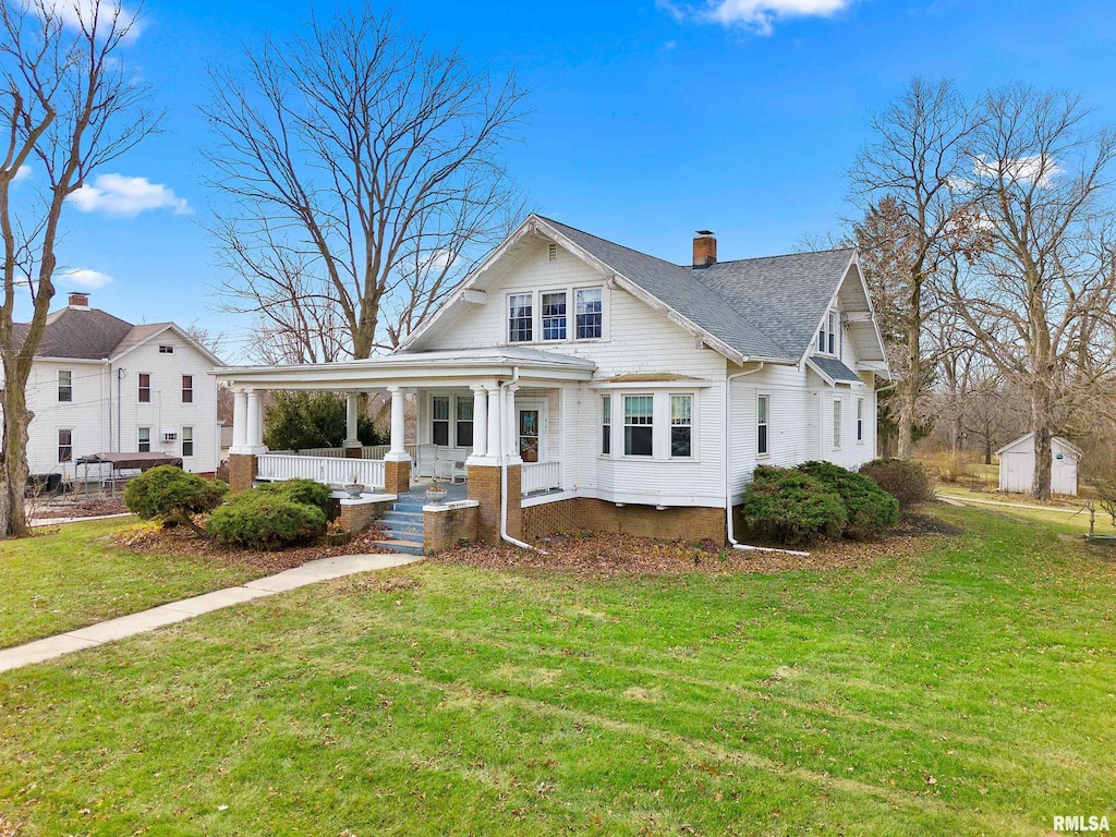 view of front of house featuring a shingled roof, a chimney, a porch, and a front yard