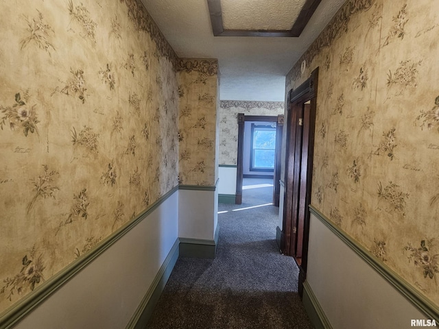 hallway with dark colored carpet, a raised ceiling, and a textured ceiling