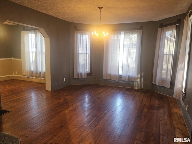 unfurnished dining area featuring dark hardwood / wood-style flooring, a textured ceiling, and an inviting chandelier