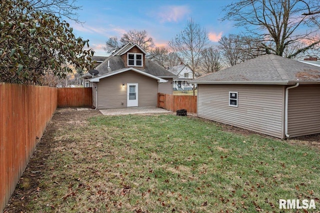 back house at dusk featuring a patio area and a lawn