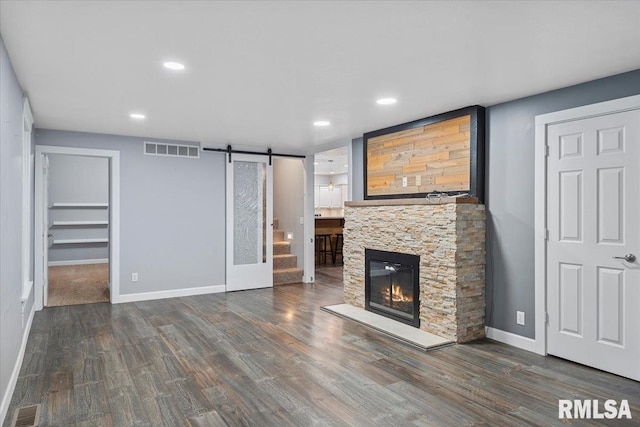 unfurnished living room featuring dark wood-type flooring, a barn door, and a stone fireplace