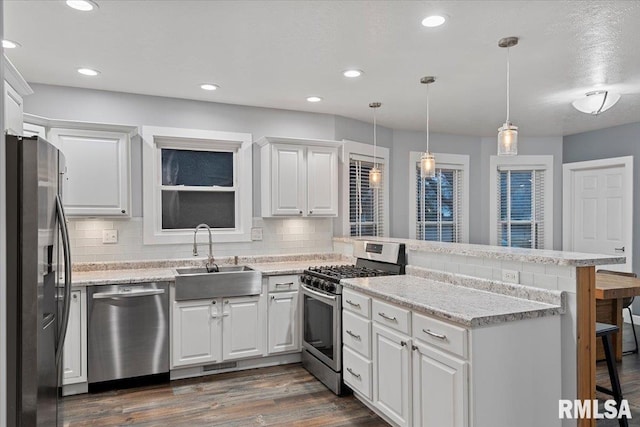 kitchen featuring decorative light fixtures, kitchen peninsula, sink, appliances with stainless steel finishes, and white cabinets