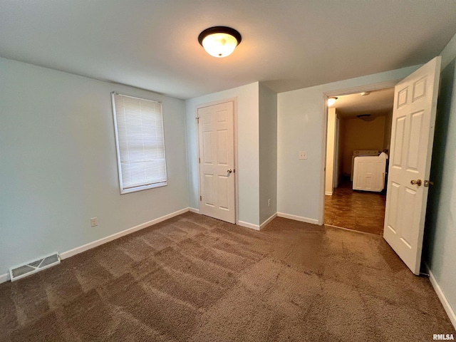 unfurnished bedroom with dark colored carpet, washer / dryer, and a closet