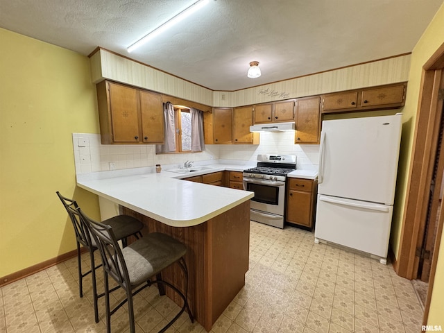 kitchen with stainless steel gas stove, kitchen peninsula, white fridge, a textured ceiling, and decorative backsplash