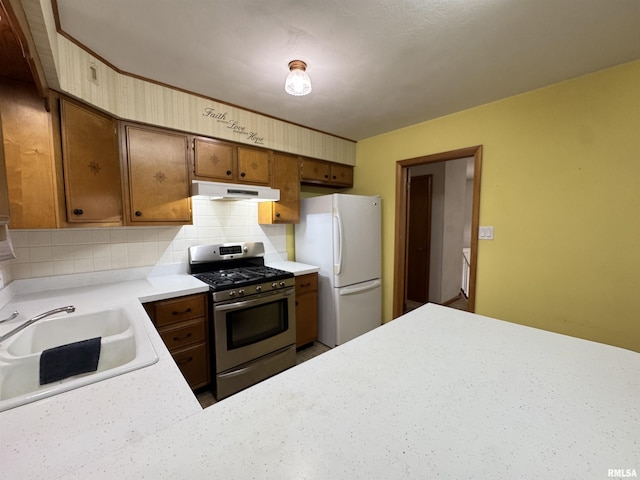 kitchen with decorative backsplash, sink, white fridge, and stainless steel range with gas stovetop