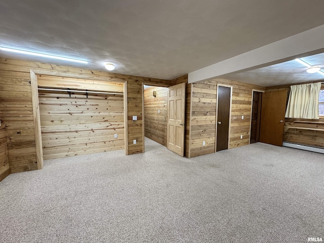 basement featuring wood walls, carpet floors, and a baseboard radiator