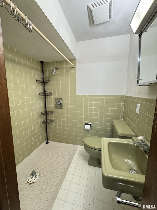 bathroom with sink, tile patterned flooring, toilet, tile walls, and a tile shower