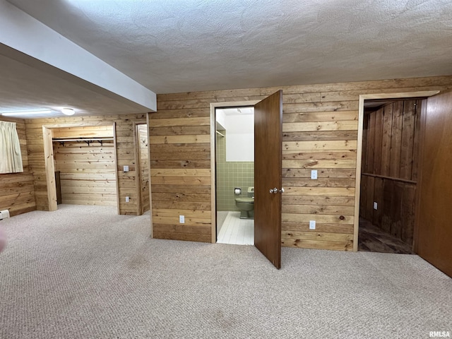 unfurnished bedroom featuring ensuite bath, wooden walls, carpet floors, and a textured ceiling