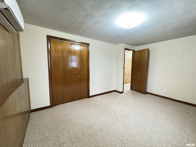 unfurnished bedroom with a wall mounted air conditioner, a textured ceiling, light colored carpet, and a closet