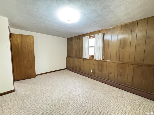 carpeted empty room featuring a textured ceiling, baseboard heating, and wooden walls