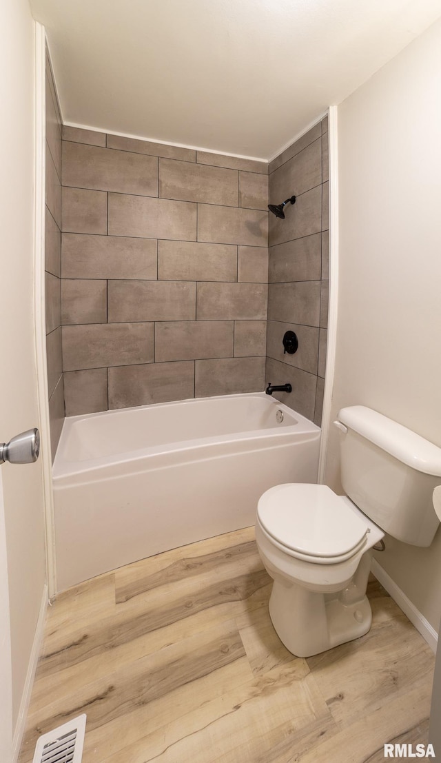 bathroom with hardwood / wood-style floors, tiled shower / bath, and toilet