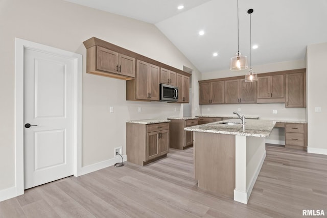 kitchen with sink, hanging light fixtures, light stone counters, light hardwood / wood-style flooring, and a center island with sink