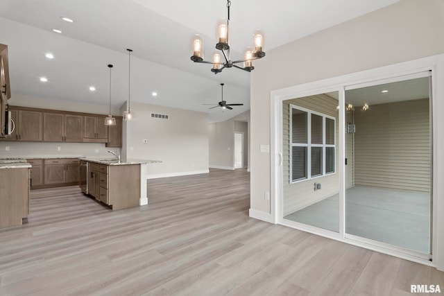 kitchen featuring light stone counters, ceiling fan with notable chandelier, an island with sink, and decorative light fixtures