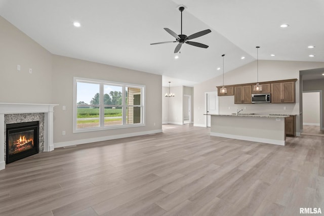 unfurnished living room featuring ceiling fan with notable chandelier, lofted ceiling, a high end fireplace, and light hardwood / wood-style flooring