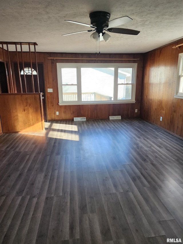 unfurnished room featuring dark hardwood / wood-style flooring, a wealth of natural light, wooden walls, and ceiling fan