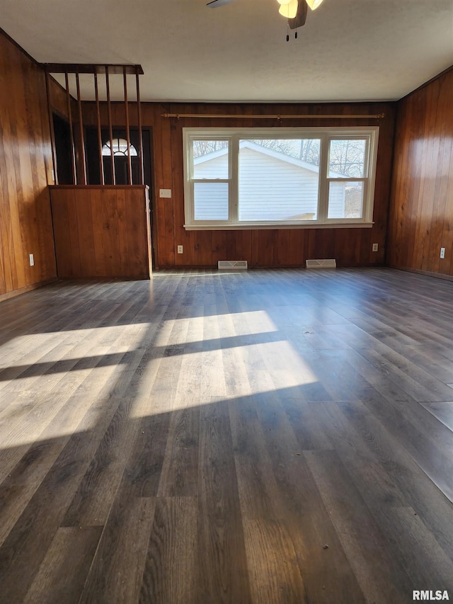 unfurnished room with dark hardwood / wood-style flooring, a wealth of natural light, wooden walls, and ceiling fan