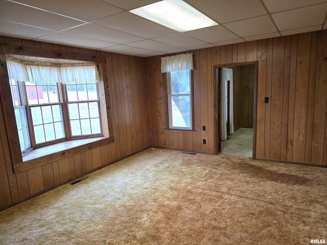 carpeted spare room with wood walls and a drop ceiling