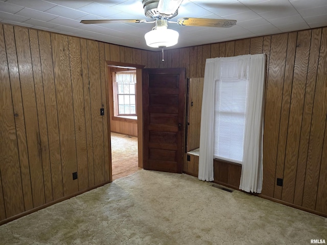 spare room with light carpet, ceiling fan, and wood walls