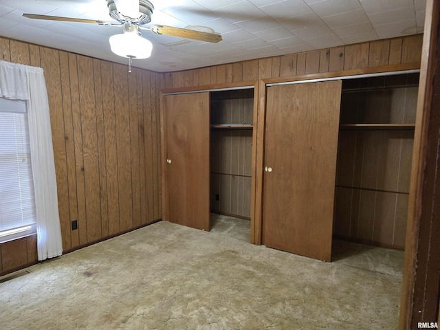 unfurnished bedroom featuring multiple closets, ceiling fan, wooden walls, and light carpet