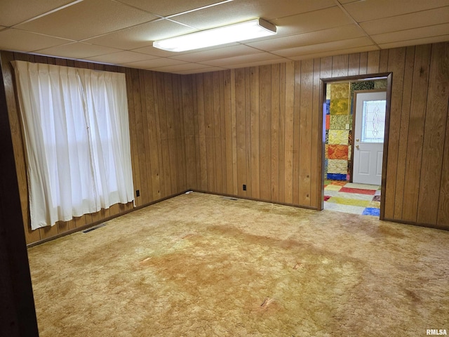 spare room featuring a paneled ceiling, light colored carpet, and wood walls