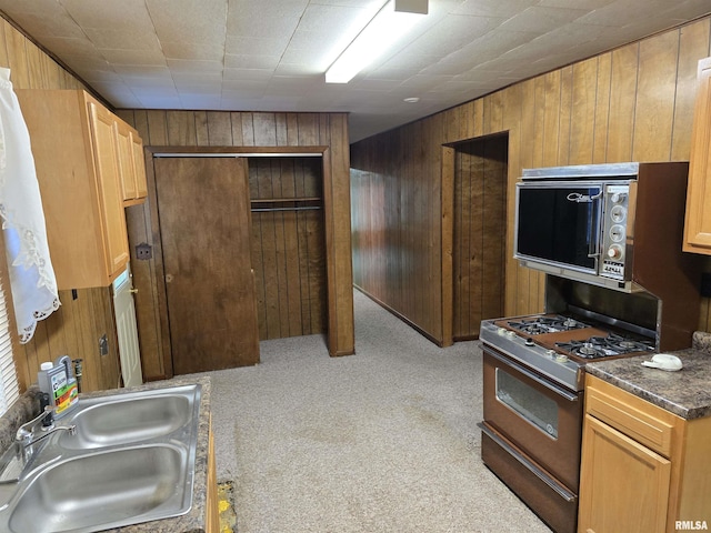 kitchen with black range with gas stovetop, wooden walls, sink, and light carpet