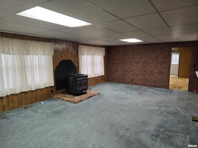 unfurnished living room with carpet flooring, a wood stove, and wooden walls