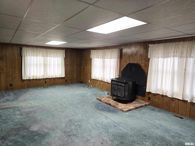 unfurnished living room featuring a wood stove, wood walls, carpet floors, and a healthy amount of sunlight