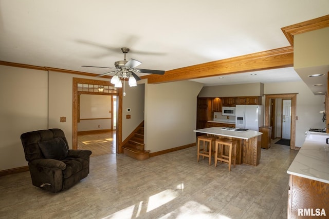 kitchen with a kitchen bar, white appliances, ceiling fan, crown molding, and a kitchen island