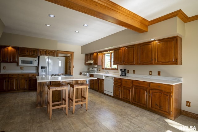 kitchen featuring sink, beamed ceiling, white appliances, a breakfast bar, and a kitchen island