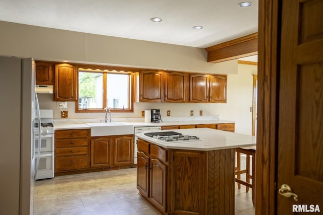 kitchen with beamed ceiling, a kitchen island, white appliances, and sink