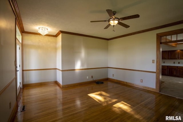 empty room with a textured ceiling, ceiling fan with notable chandelier, wood-type flooring, and crown molding