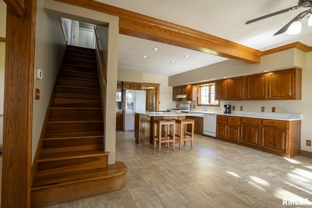 kitchen with white appliances, ceiling fan, beam ceiling, a kitchen island, and a breakfast bar area